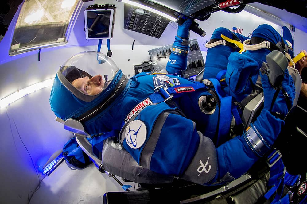Un astronauta en el traje azul de Boeing reclinado en una de las sillas de la Starliner con los paneles de control frente a él y su mano derecha sujetando la palanca de control