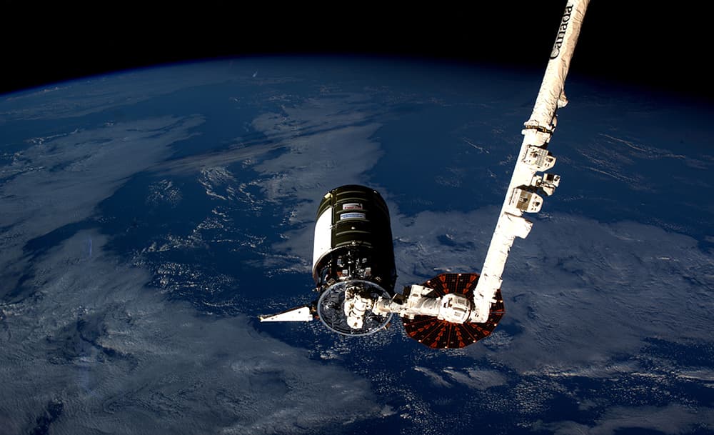 La Cygnus 18 capturada por el brazo robot de la Estación con la Tierra al fondo. La foto muestra como uno de los paneles solares está abierto y el otro no