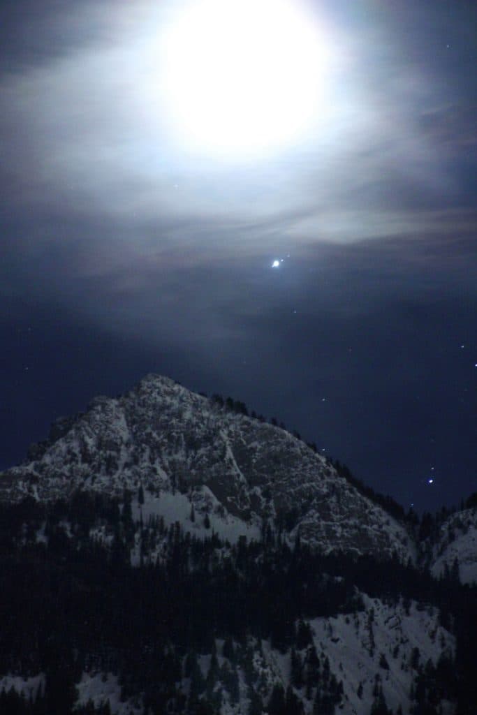 La luna y Júpiter y tres de sus lunas sobre las montañas Wasatch en una imagen nocturna. La Luna está sobreexpuesta para que se vean el planeta y sus lunas