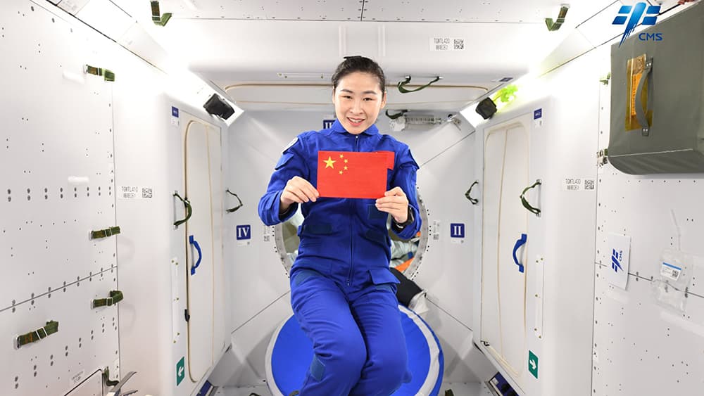 Liu Yang en el centro de la imagen con un mono de vuelo azul sostiene una bandera china en las manos