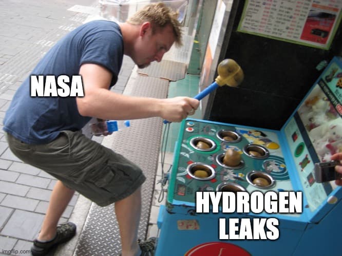 Foto de un tipo jugando al Whak-A-Mole en la que a él le han superpuesto un rótulo que dice «NASA» y a los tops uno que dice «fugas de hidrógeno»