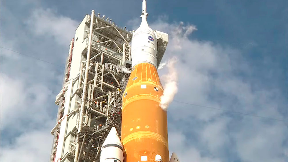 La parte superior de la primera etapa, la segunda etapa, y la cápsula Orión, con la torre de lanzamiento al fondo, en esta imagen en la que se ve como el cohete purga oxígeno e hidrógeno en forma de vapor al tener los depósitos ya llenos