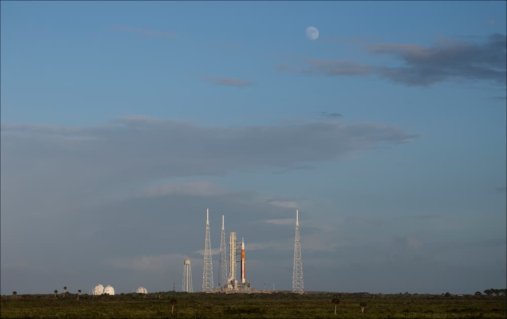 Vista lejana de la plataforma de lanzamiento con el SLS en ella y la Luna en el cielo