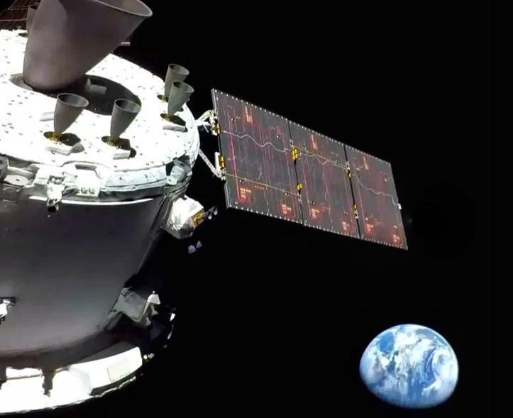 La Tierra flota en el negro del espacio vista desde la cápsula Orión, de la que se ven los motores de la parte inferior del módulo de servicio y uno de sus paneles solares