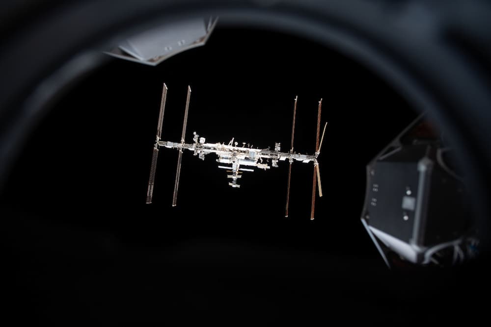 La EEI recortada contra la negurar del espacio visto a través de la escotilla superior de la Endeavour, cuyo perfil y pétalos de contacto con la Estación se ven en el borde de la foto