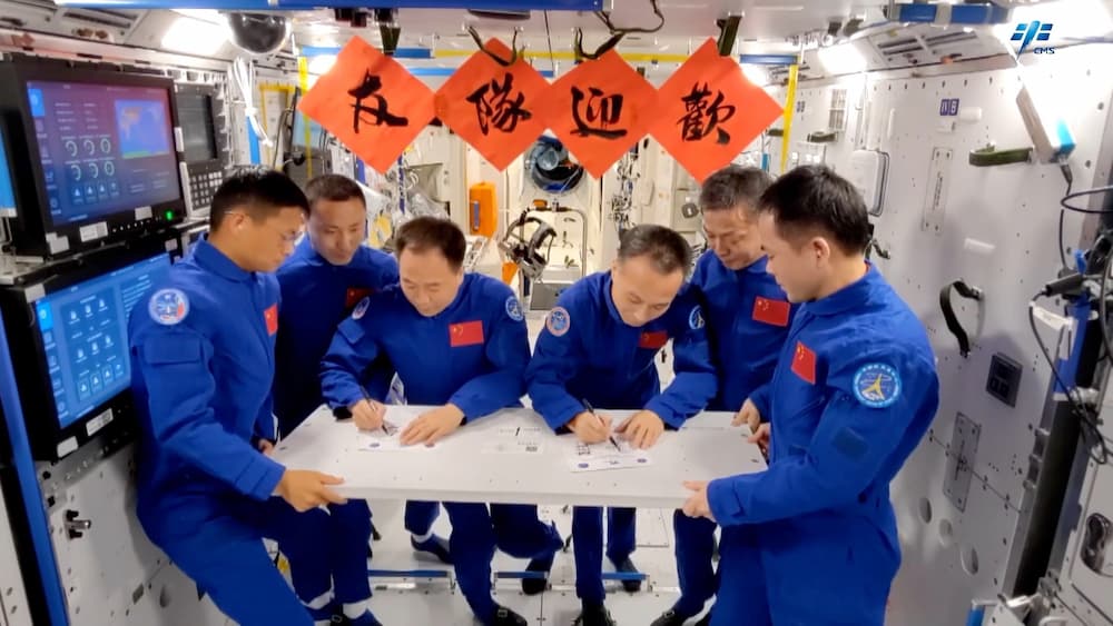 Los comandantes de la Shenzhou 15 y 16 firman los documentos para transferir el mando de la estación sobre un tablero que sujetan los otros cuatro tripulantes
