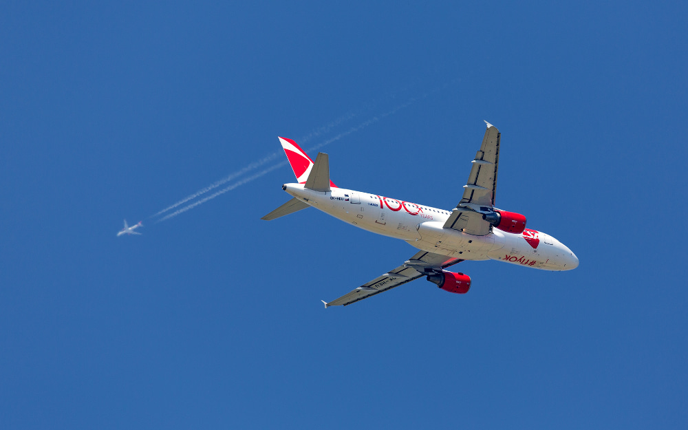 El avión recortado contra un cielo azul; mucho más arriba se ve otro avión viajando en dirección contraria dejando estelas de condensación