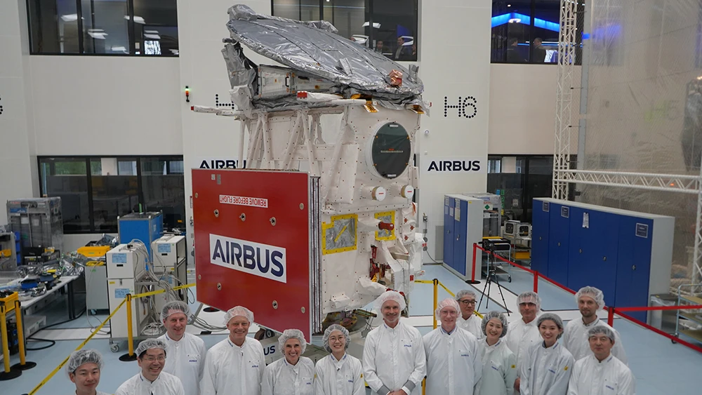 El satélite en una sala limpia junto con unas personas para dar una idea de su tamaño