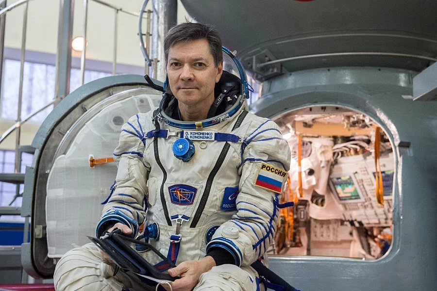 Retrato de medio cuerpo de Kononenko con su traje espacial frente al simulador de la cápsula Soyuz