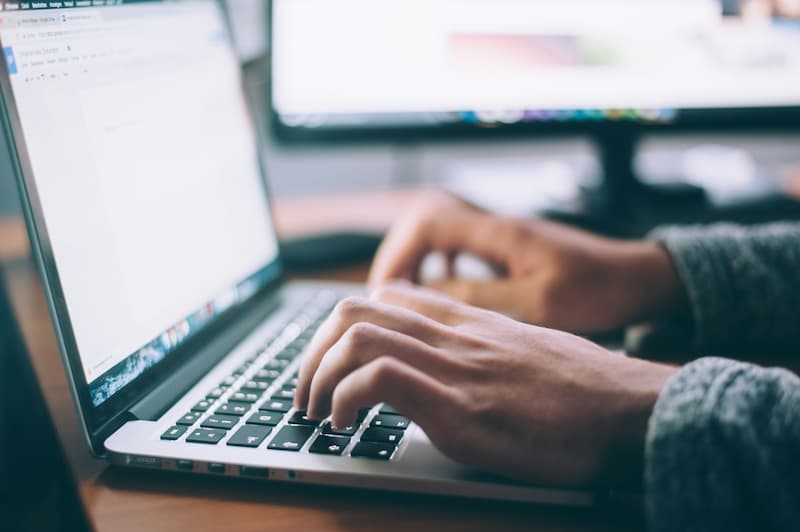 Manos escribiendo en un ordenador portátil, con la pantalla mostrando un documento de texto. Foto (CC) Glenn Carstens-Peters @ Unsplash