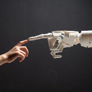 Contacto Una mano robot y una mano humana cuyos dedos índices están a punto de tocarse como en La Creación de Adán de Miguel Ángel