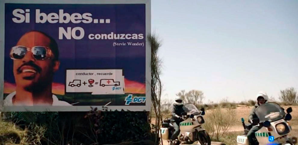 Imagen con una valla publicitaria de la campaña «Si bebes no conduzcas» y dos motoristas de la Guardia Civil al lado