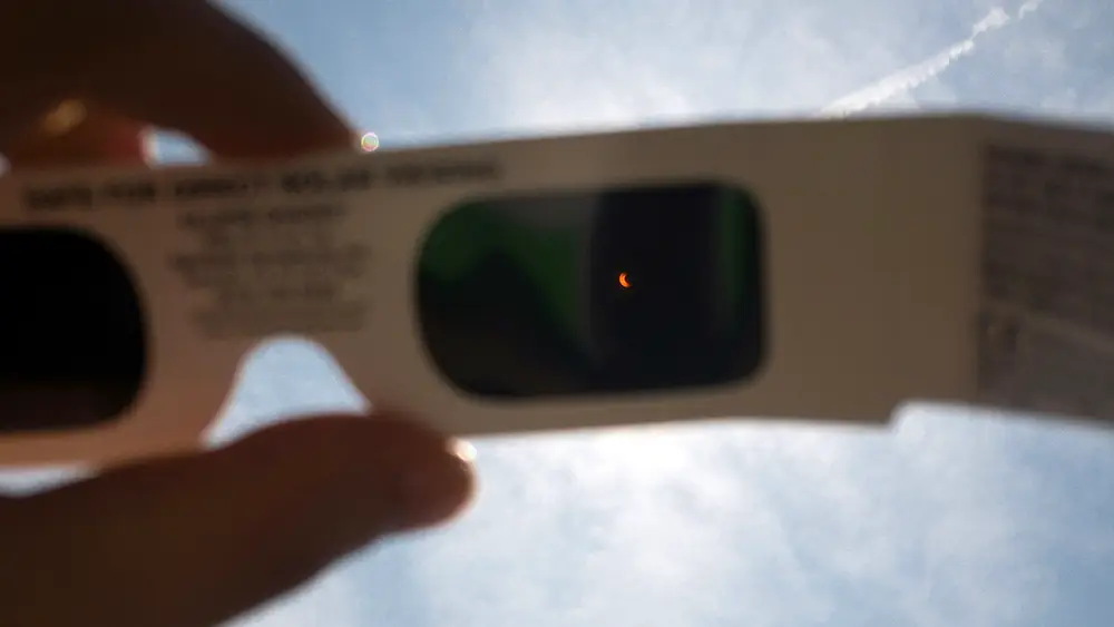 El Sol visto a través de unas gafas para eclipses sujetas por una mano